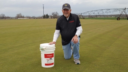 Richard Hurley GSNB’83 at the East Coast Sod & Feed farm in Salem County, New Jersey, with a bucket of turfgrass seed he developed.